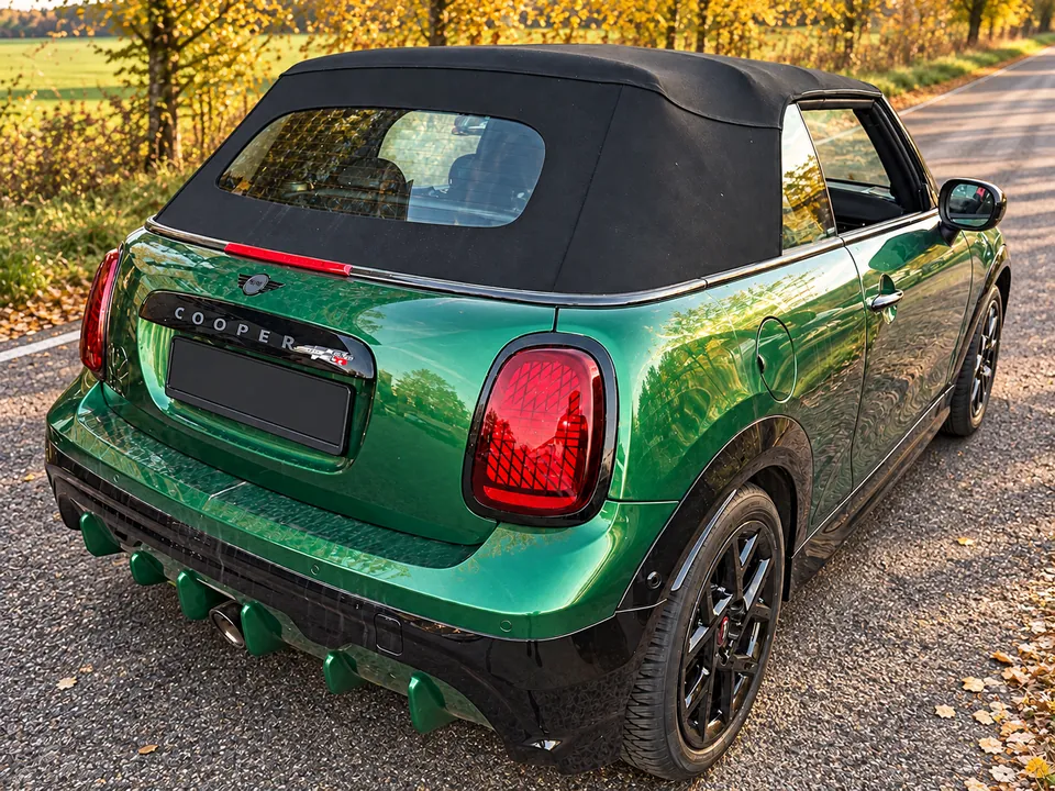 Grüner MINI Cabrio JCW auf einer herbstlichen Landstraße, schräge Heckansicht mit geschlossenem Stoffverdeck